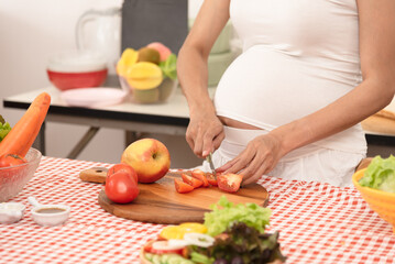 Obraz na płótnie Canvas Happy pregnant woman cooking at home, preparing fresh green salad, eating many different vegetables good for pregnancy, healthy pregnancy concept