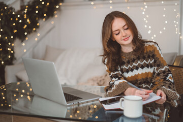 Portrait of smiling woman working on laptop or shopping online, buying new year presents with decorated Christmas tree on background, typing on keyboard.
