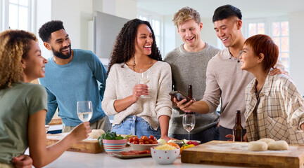 Group Of Friends At Home In Kitchen Making Food For Party Looking At Recipe On Mobile Phone