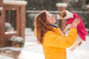 Caucasian woman hugging with dog while walking in winter. Jack Russell Terrier in a warm pink...