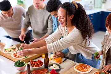 Group Of Friends At Home In Kitchen Adding Toppings To Homemade Pizzas For Party Together