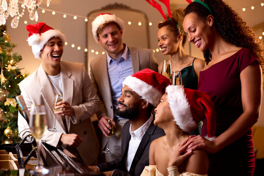Friends At Piano Wearing Santa Hats And Reindeer Antlers Celebrating At Christmas Or New Year Party