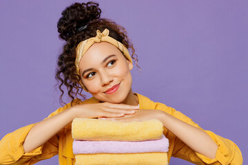 Young housekeeper woman wears yellow shirt tidy up hold put hands on pile of clothes t-shirts look aside on workspace area isolated on plain pastel light purple background studio. Housework concept.