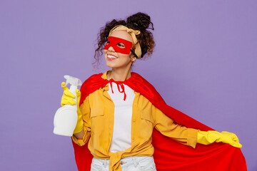 Young housekeeper woman wear yellow shirt rubber gloves red super hero cloak mask hold detergent...