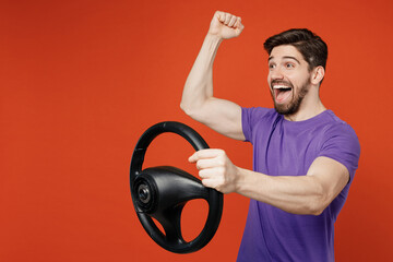 Side view young overjoyed brunet man wear casual basic purple t-shirt hold steering wheel driving car do winner gesture isolated on plain orange background studio portrait. People lifestyle concept.