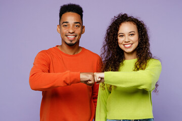 Young smiling happy couple two friends family man woman of African American ethnicity wearing casual clothes together meet each other give fist bump isolated on pastel plain light purple background.