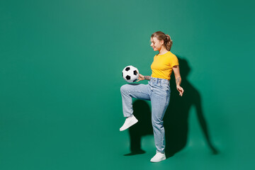 Fototapeta na wymiar Side profile view full body young woman fan wear basic yellow t-shirt cheer up support football kick soccer ball on knee doing exercise watch tv live stream isolated on dark green background studio.