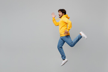Full body side view overjoyed excited fun cool young Indian man 20s he wearing casual yellow hoody run fast hurry up isolated on plain grey color background studio portrait. People lifestyle portrait.