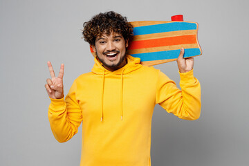 Young smiling happy fun cool cheerful Indian man 20s he wearing casual yellow hoody hold skateboard...
