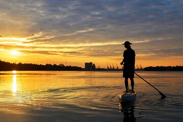 Silhouette of a man with a paddle on a SUP (stand up paddle board) at early sunny morning on river....