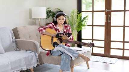 Woman practicing or learning to play guitar and practice using his fingers to hold guitar chords while looking at music notes with intention, Taking advantage of free time, Relax during free time.
