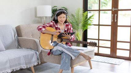 Woman practicing or learning to play guitar and practice using his fingers to hold guitar chords while looking at music notes with intention, Taking advantage of free time, Relax during free time.