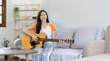Asian female artist playing the guitar and singing happily in the living room, Relaxation with...