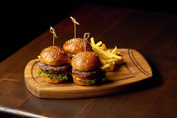 American fast food: three small cheeseburgers on a board. Dark wooden background. Finger food