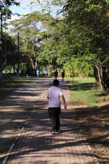 Elderly man walks alone on walking path in park on sunny day