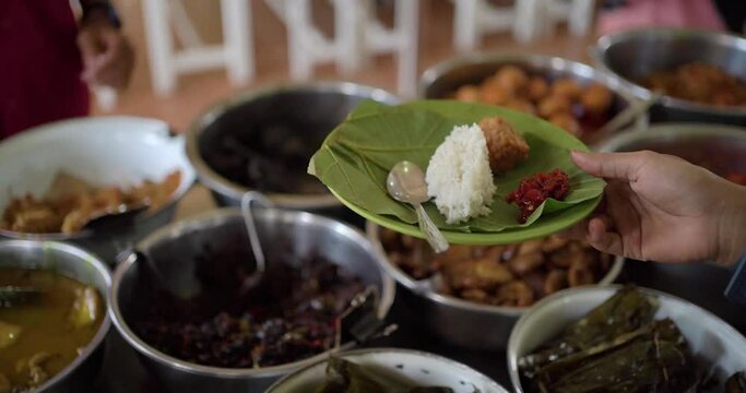 typical culinary Nasi Jamblang favorite villagers from Cirebon. The waiter is taking tempeh, fried prawns that have been topped with rice and chili sauce on teak leaf plates and given to customers