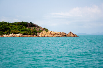 Tropical island with trees and rocky cliff in turquoise color sea