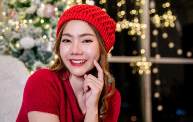 Portrait of beautiful Asian woman in red sweater hat, warm and cozy evening in Christmas interior design. Christmas xmas decoration wear red winter warm wool sweater.Beauty skin, facial cosmetic.