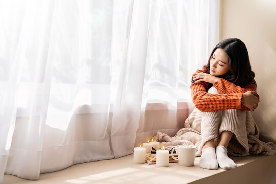 Asian sad lonely alone woman warm up of coffee and candle cozy bed with book and blanket. Warm woolen sweater in cold autumn or winter weekend, warm drink. Lazy day, Cosy scene, hygge concept banner