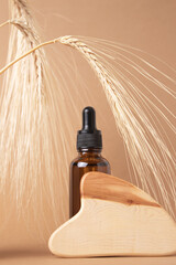 Fototapeta premium Bottle with lotion, serum, essential oil with wooden guasha on a beige background. Natural organic eco cosmetics. Natural cosmetics made from wheat and barley.
