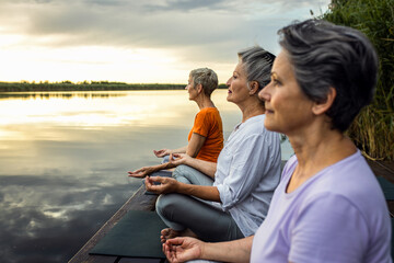 Group of senior woman doing yoga exercises by the lake.