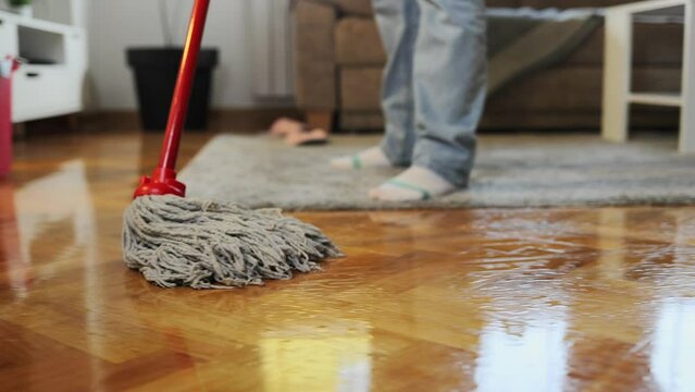 Cleaning service. Housewife mopping parquet with wet mop. Close-up of washing floor. Follow shot. Low angle view.