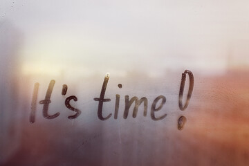 Hand drawn message Its time on foggy glass on city sunset window