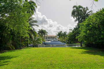 View of a yacht with cover from a yard with green lawn and fence at the bay in Miami, Florida