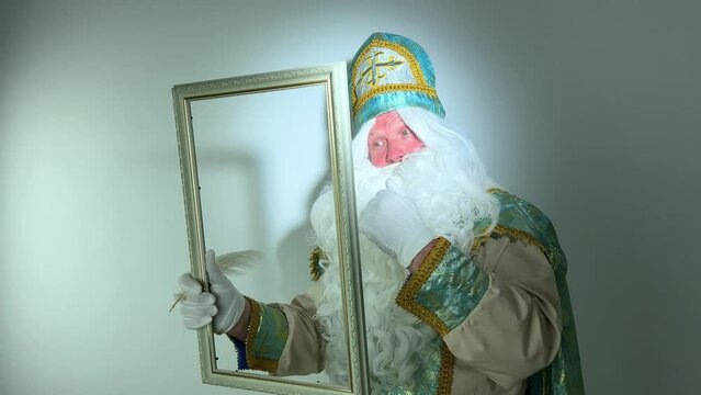 saint nicholas draws in an empty frame with a beautiful white pen a fabulous letter magical action he has a white fluffy beard a suit blue with gold he comes before santa claus