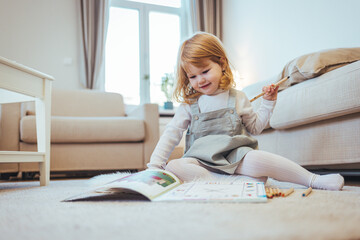 Kindergarten children education, or preschool child study at home concept. Close up photo of a blonde little girl drawing something in her notebook sitting at the table in the kitchen