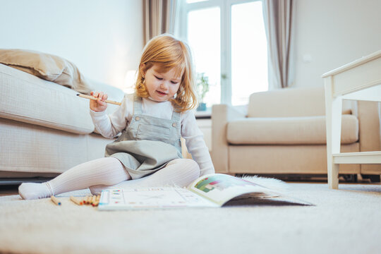 Kindergarten children education, or preschool child study at home concept. Close up photo of a blonde little girl drawing something in her notebook sitting at the table in the kitchen