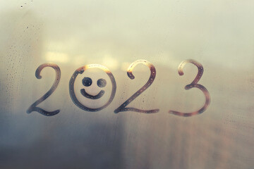 numbers 2023 of new year with smile face paint on splashed by rain foggy glass on blue sunset window