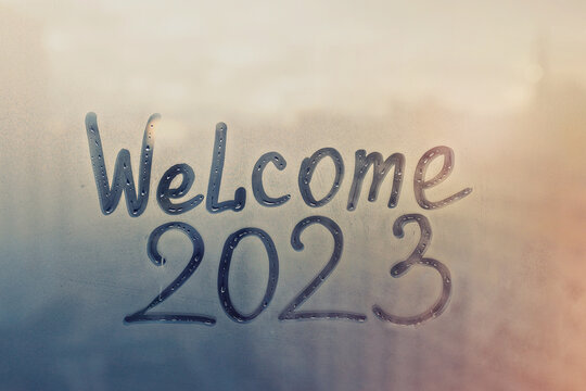 lettering Welcome and numbers 2023 of new year paint with finger on splashed by rain foggy glass on blue and sunset window