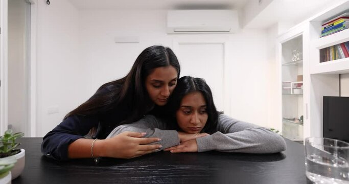 Young woman consoling sad friend embracing her in living room