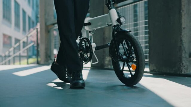 Close up of the businessman feets going to the workplace and carrying the electro vehicle near him. Male boss near business centre with his electro bicycle. People, technology, transportation concept.