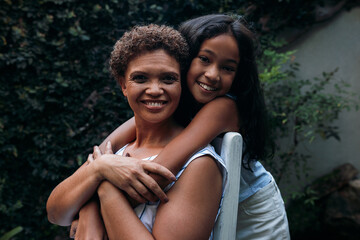 Fototapeta premium Portrait of a girl and her grandmother. Granny sitting on a chair granddaughter hugging her from back.