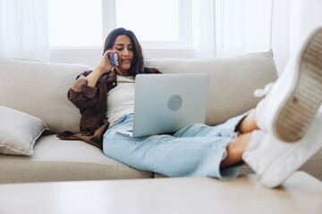 Woman blogger with phone lying at home and talking on the phone on sofa with laptop and working freelancer online, selfie