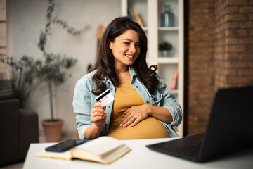 Pregnant woman shopping online at home. Happy woman with laptop and credit card...