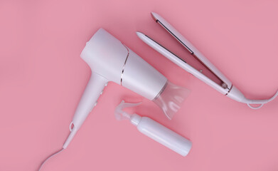 Fototapeta premium Top view of a hair straightener and hair dryer on a pink background. Hair care concept. light hair dryer