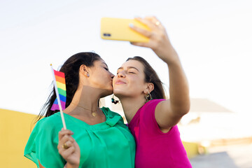 A beautiful lesbian young couple embraces and holds a rainbow flag. Girls taking selfie photo