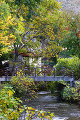 Small rustic bridge crossing the river and colorful autumn leaves. Beautiful autumnal landscape.
