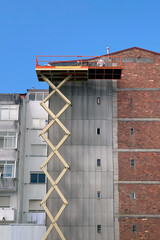 workers on the industrial elevator repair the facade of a residential building