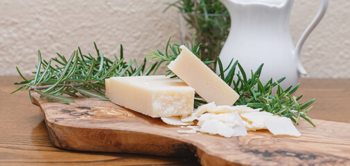 Pieces of parmigiano reggiano or parmesan cheese on wooden cutting board with rosemary.Top Italian...