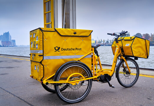 Deutsche Post bicycle in yellow with large container for letters and parcels stands on a pier in the port of Hamburg, Germany, November 14, 2022