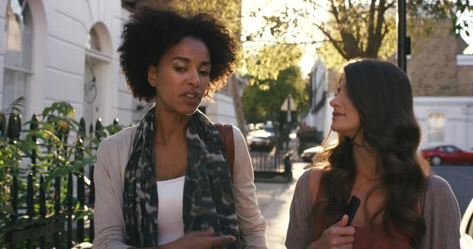 Women, talking and phone while walking on city street in relax bonding, travel sightseeing or after work commute. Black woman, people or fashion friends on mobile technology in London location street