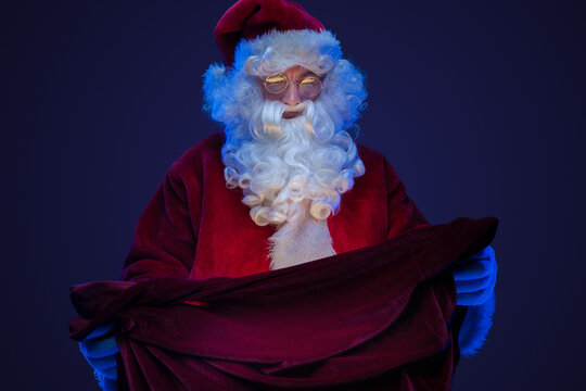 Shot of santa claus dressed in red suit looking at bag with gifts.