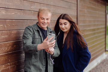 Portrait of two friends using cellphone and listening to music on the street