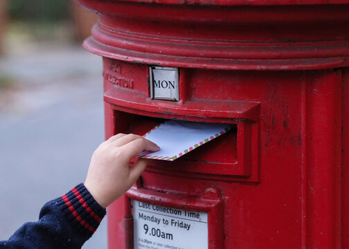 Child Is Posting A Letter Into The Classic Red English Postbox. 