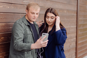 Portrait of two friends using cellphone and listening to music on the street