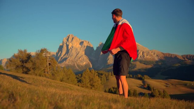 Mountains, forest and grass fields with a man holding an Italian flag filmed at Alpe di Siusi in Alps, Italian Dolomites filmed at sunset. Filmed at tight focall lenghtclose to gorund, slow motion 4k